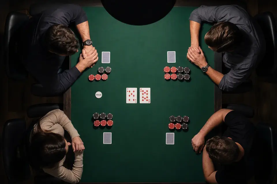 patru jucători la o masă de poker cu fetru verde, cu jetoane stivuite și cărți comune pe masă